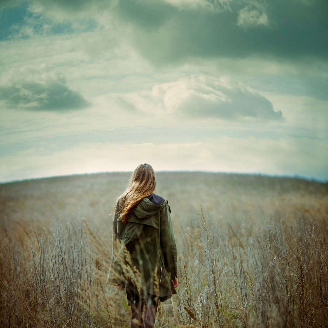 Woman standing alone in a field looking toward the horizon